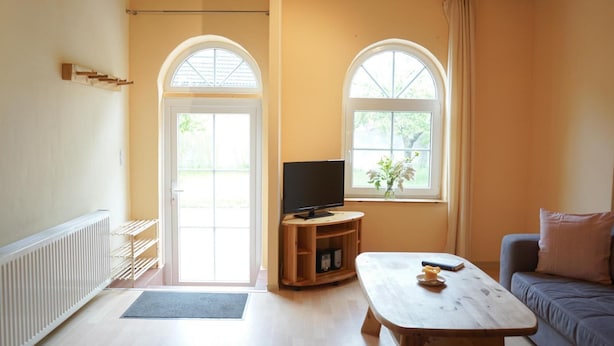 Una sala de estar con televisión, sofá, mesa de centro y dos ventanas.