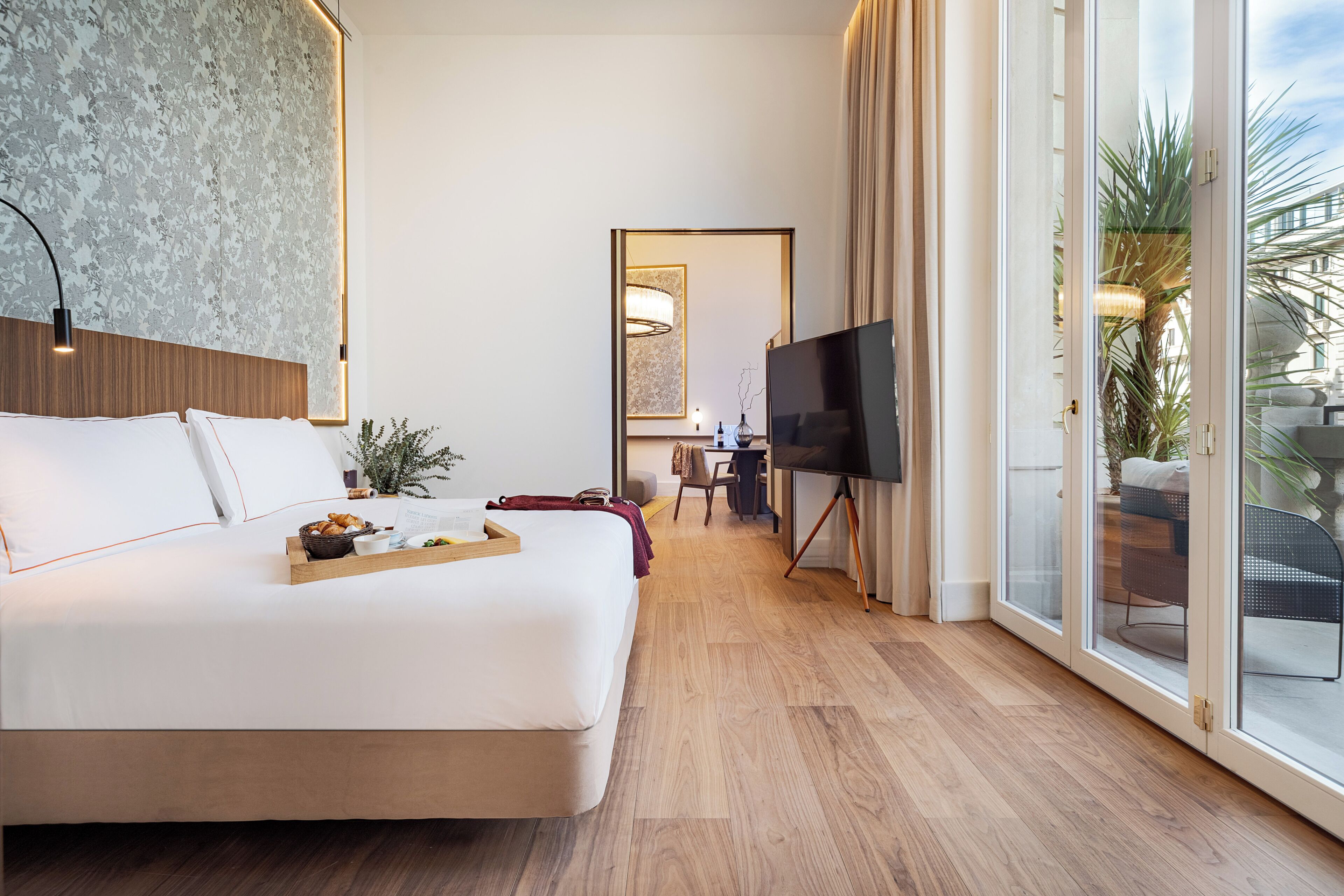 A modern hotel room with a large bed, a TV, a desk, and a view of the outdoors.