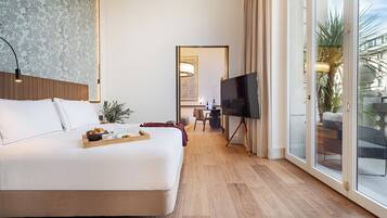 A modern hotel room with a large bed, a TV, a desk, and a view of the outdoors.