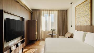 A hotel room with a large bed, a television, a desk, and a window with curtains.
