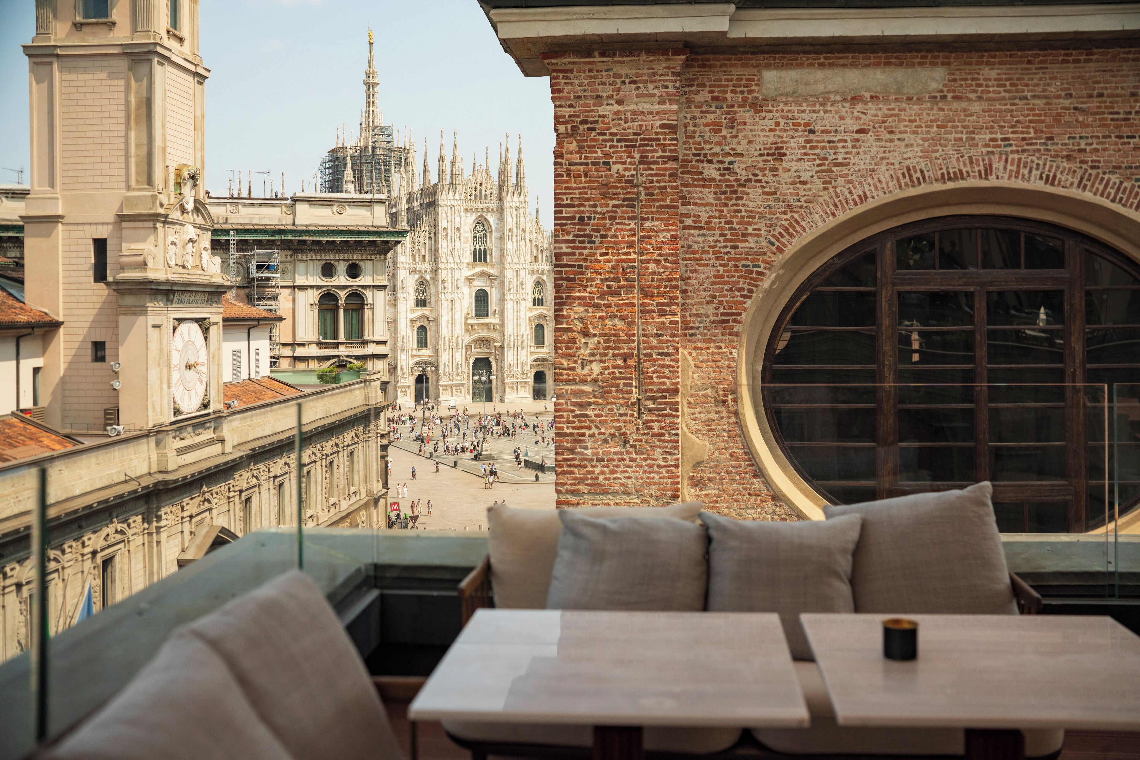 A view from a balcony with a table and chairs, overlooking a historic building with a clock tower and a large cathedral.