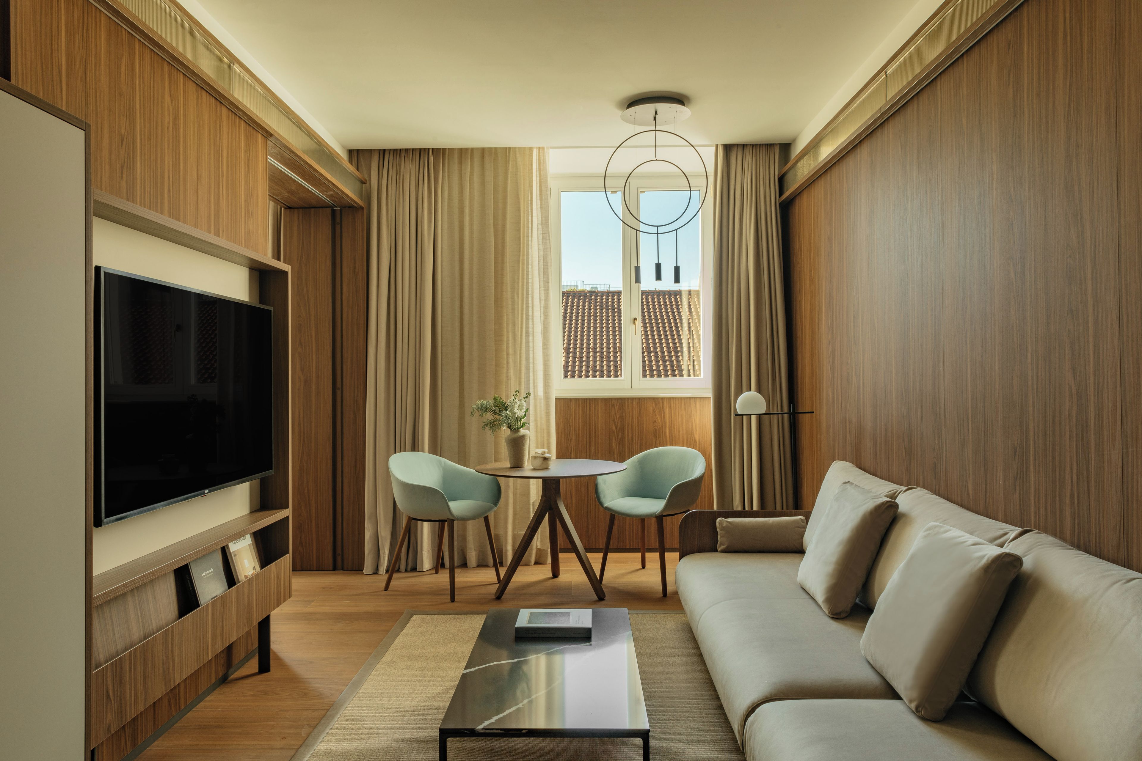 A modern living room with a flat-screen TV, a sofa, a coffee table, and a dining area with two chairs.