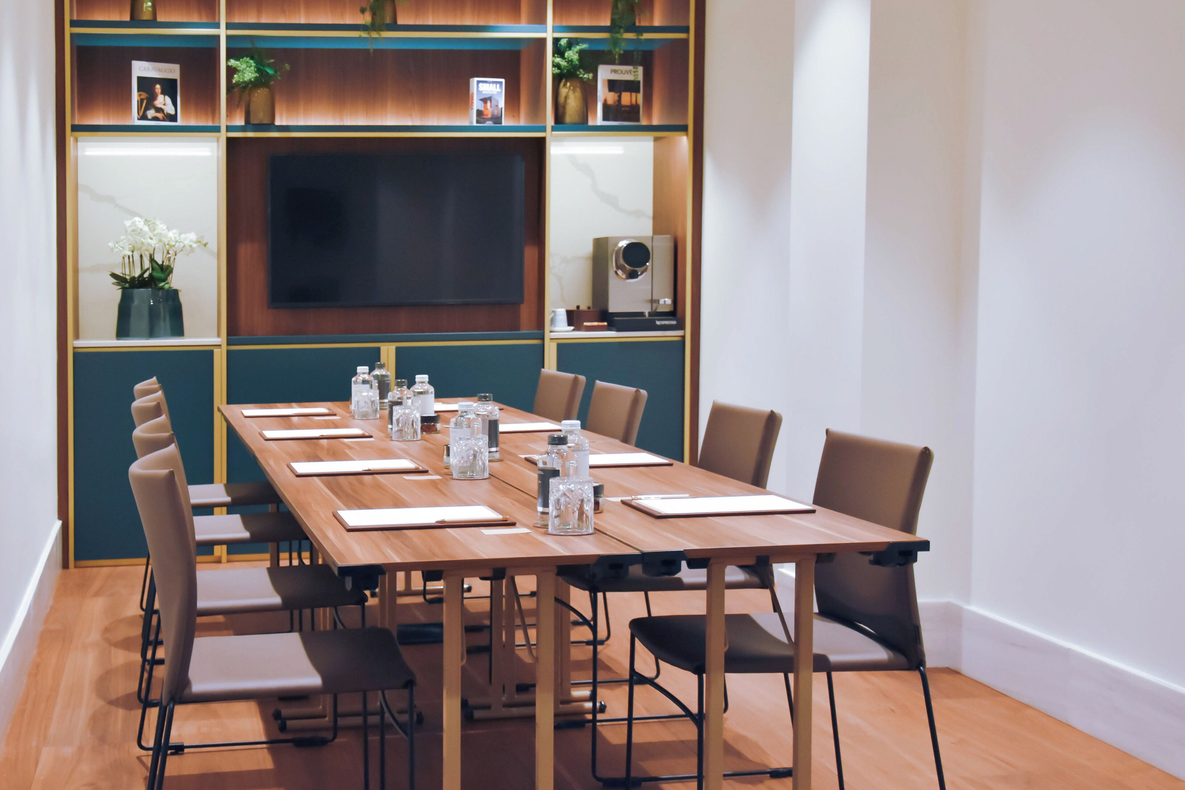 A conference room with a long table, chairs, a TV screen, and decorative items on shelves.