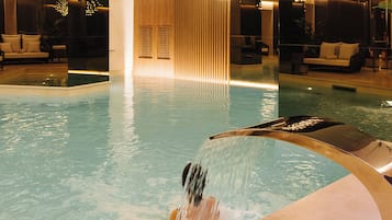 Piscina interior moderna con cascada, rodeada de zonas de descanso e iluminación contemporánea.