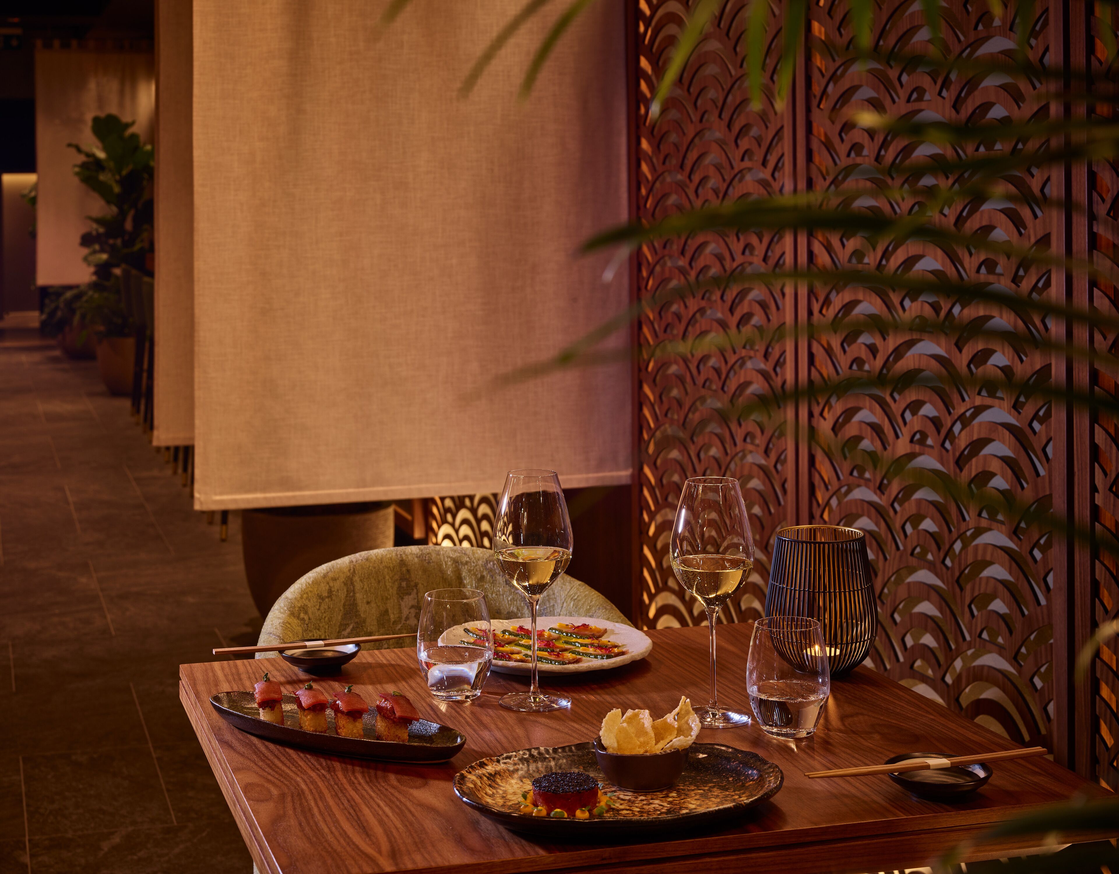 A dining table with plates of food, glasses of water and wine, and chopsticks.