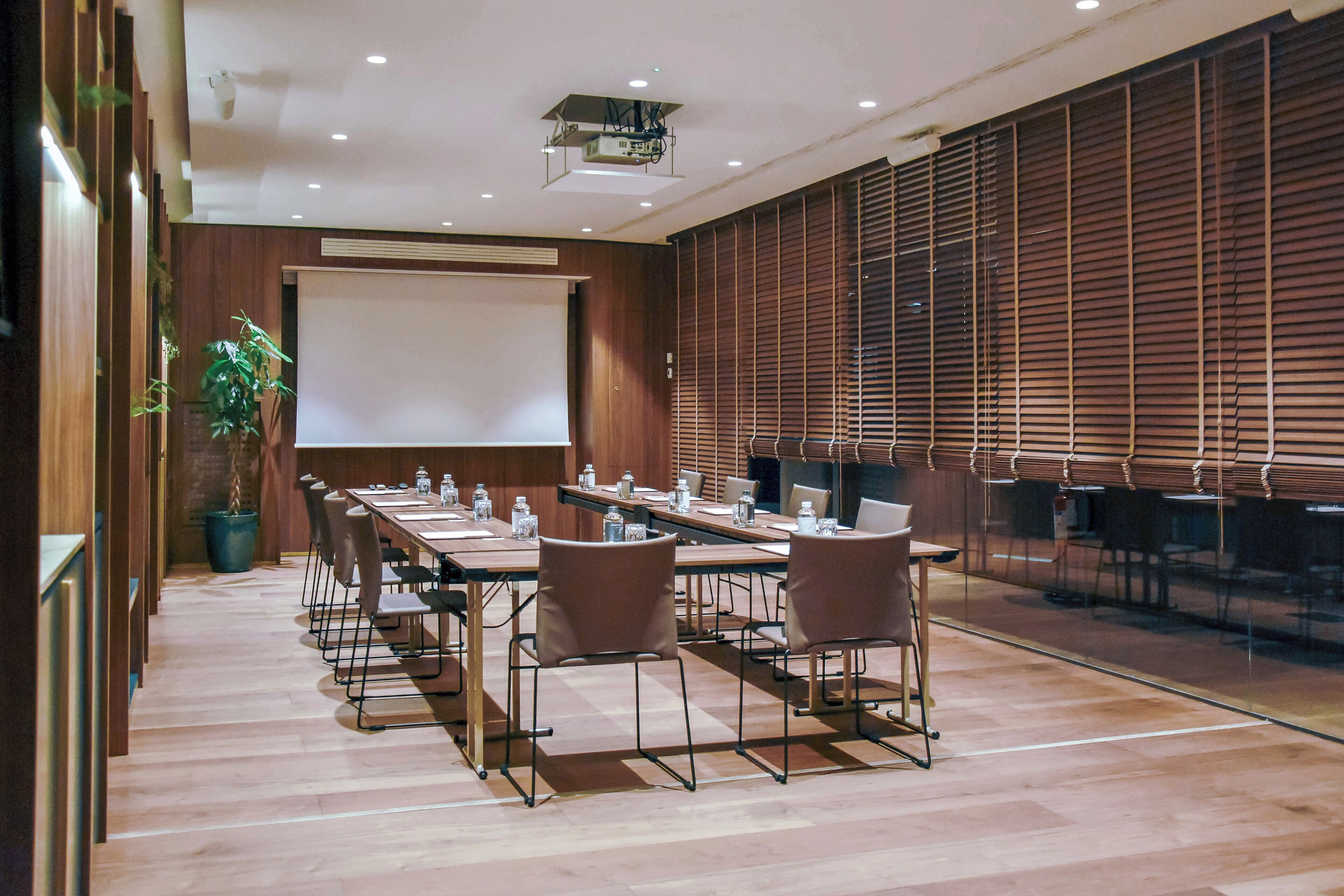 A conference room with a long table, chairs, a projector screen, and a large window with blinds.