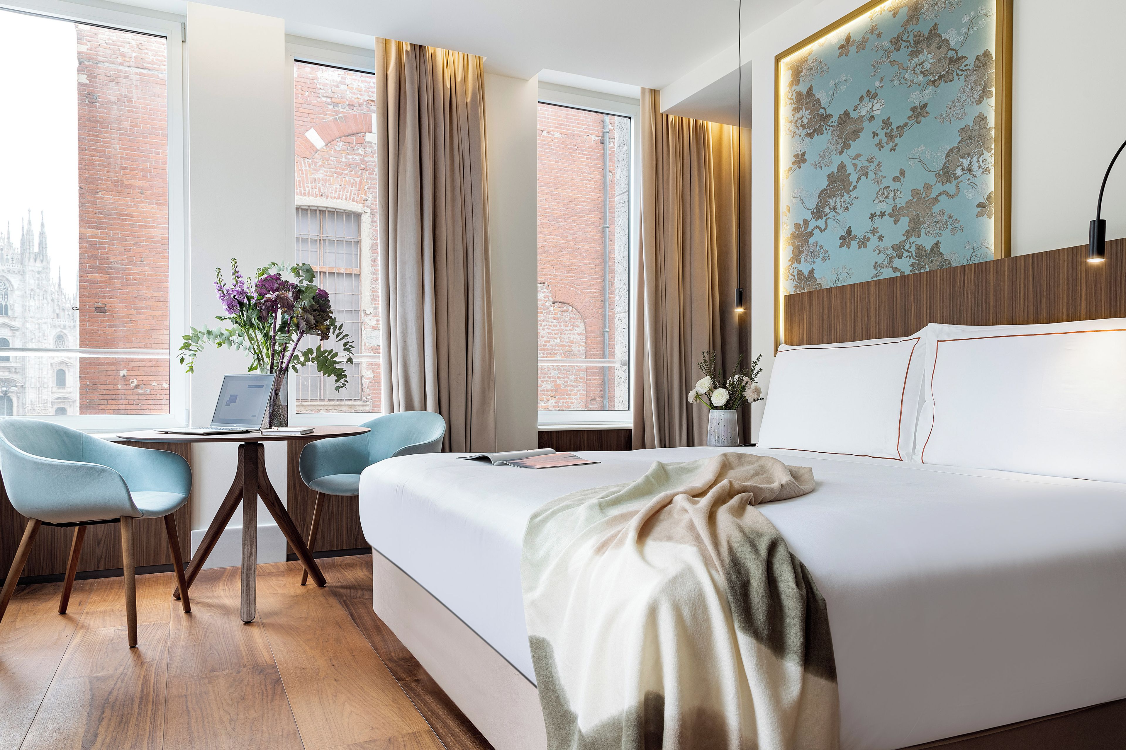 Une chambre d’hôtel avec un grand lit, un bureau avec deux chaises, un ordinateur portable et un vase rempli de fleurs.