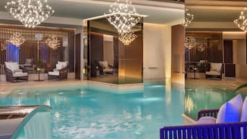 Un área de piscina interior moderna con una barrera de cristal, sillones de descanso e iluminación decorativa.