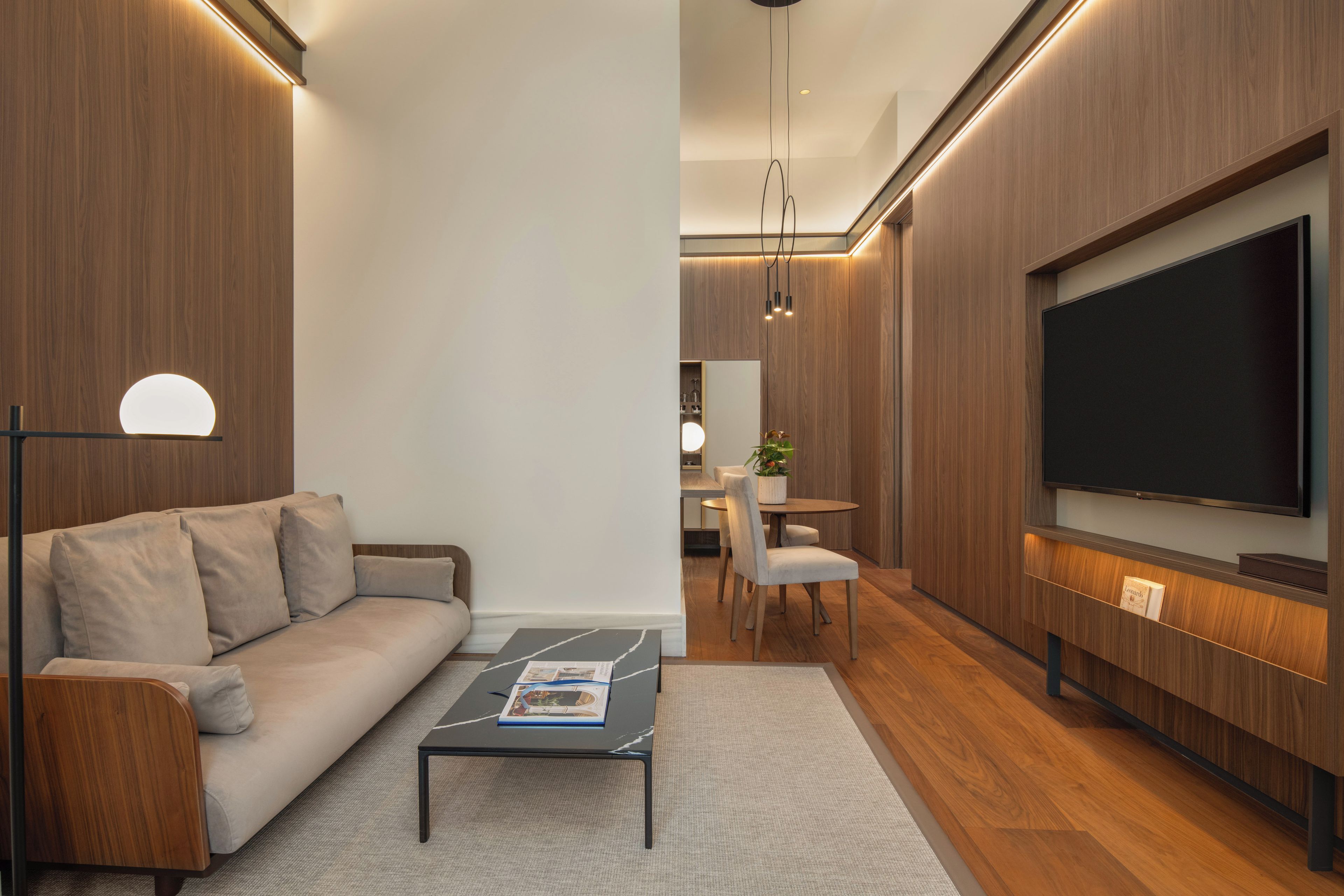 A modern living room with a sofa, coffee table, TV, and dining area.