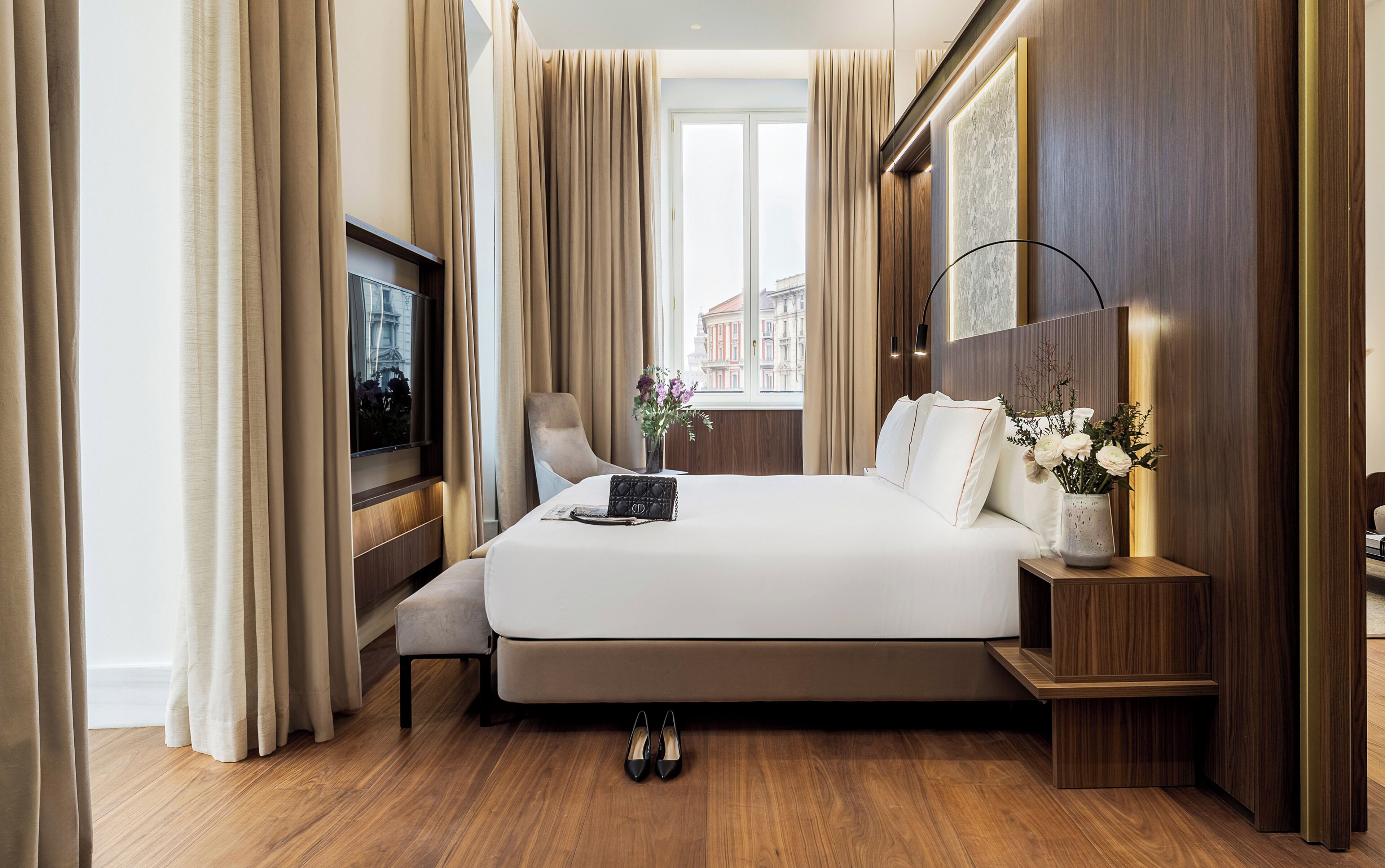 Camera d'albergo con un letto grande, una televisione, una sedia, un comodino e una finestra con tende.