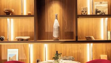 Un interior de madera con una mesa redonda, dos sillas rojas y estantes con diversos objetos decorativos.