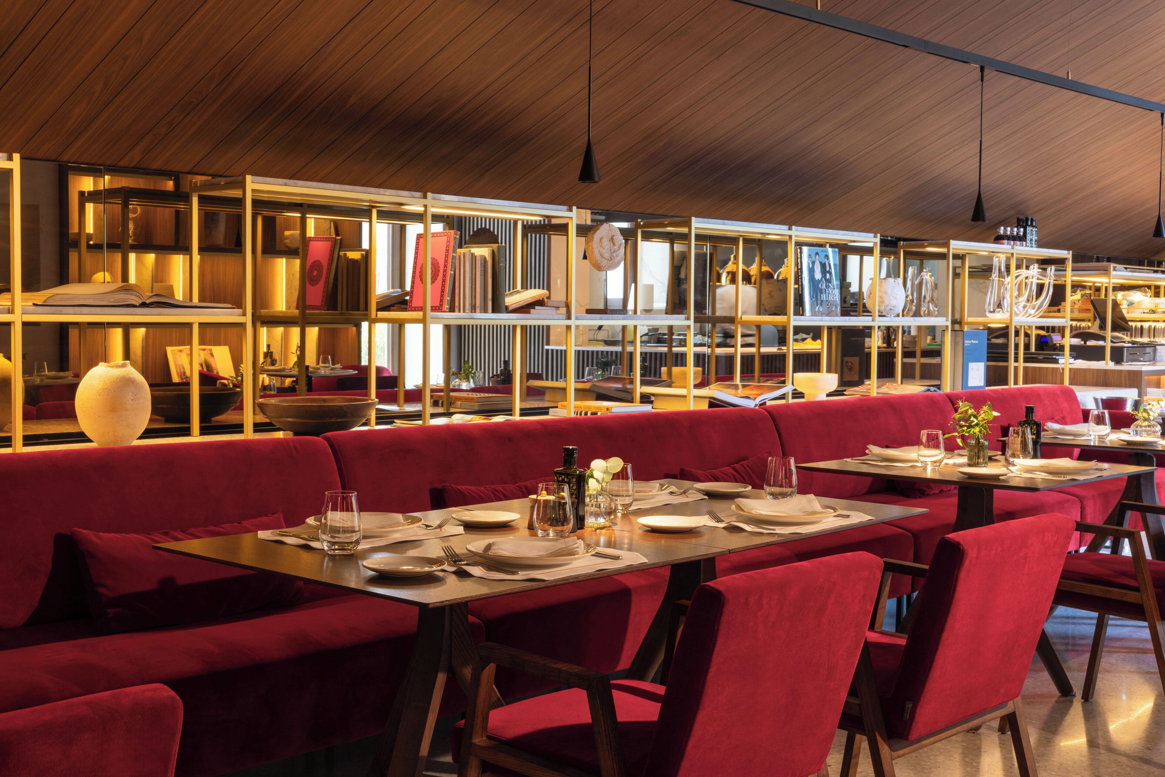 A restaurant with red upholstered booths and tables, wooden ceiling, and shelves with books and decorative items.