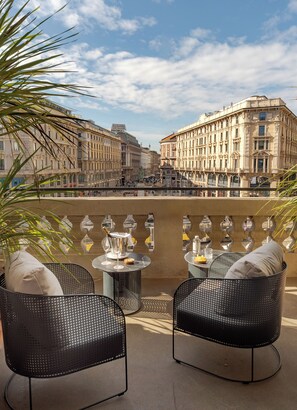 A terrace with two wicker chairs, a small round table, and a bottle of champagne. In the background, there is a large building with classical architecture. - Palazzo Cordusio Gran Meliá – The Leading Hotels of the World (Milan)