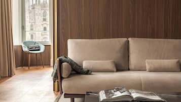 A modern living room with a beige sofa, a small table with a magazine, and a view of a historic building through a window.