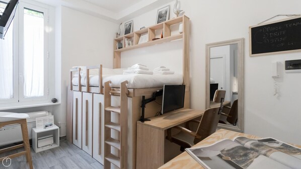 Habitación compacta y bien organizada, con una litera, un escritorio con computadora y un pequeño espacio de trabajo.