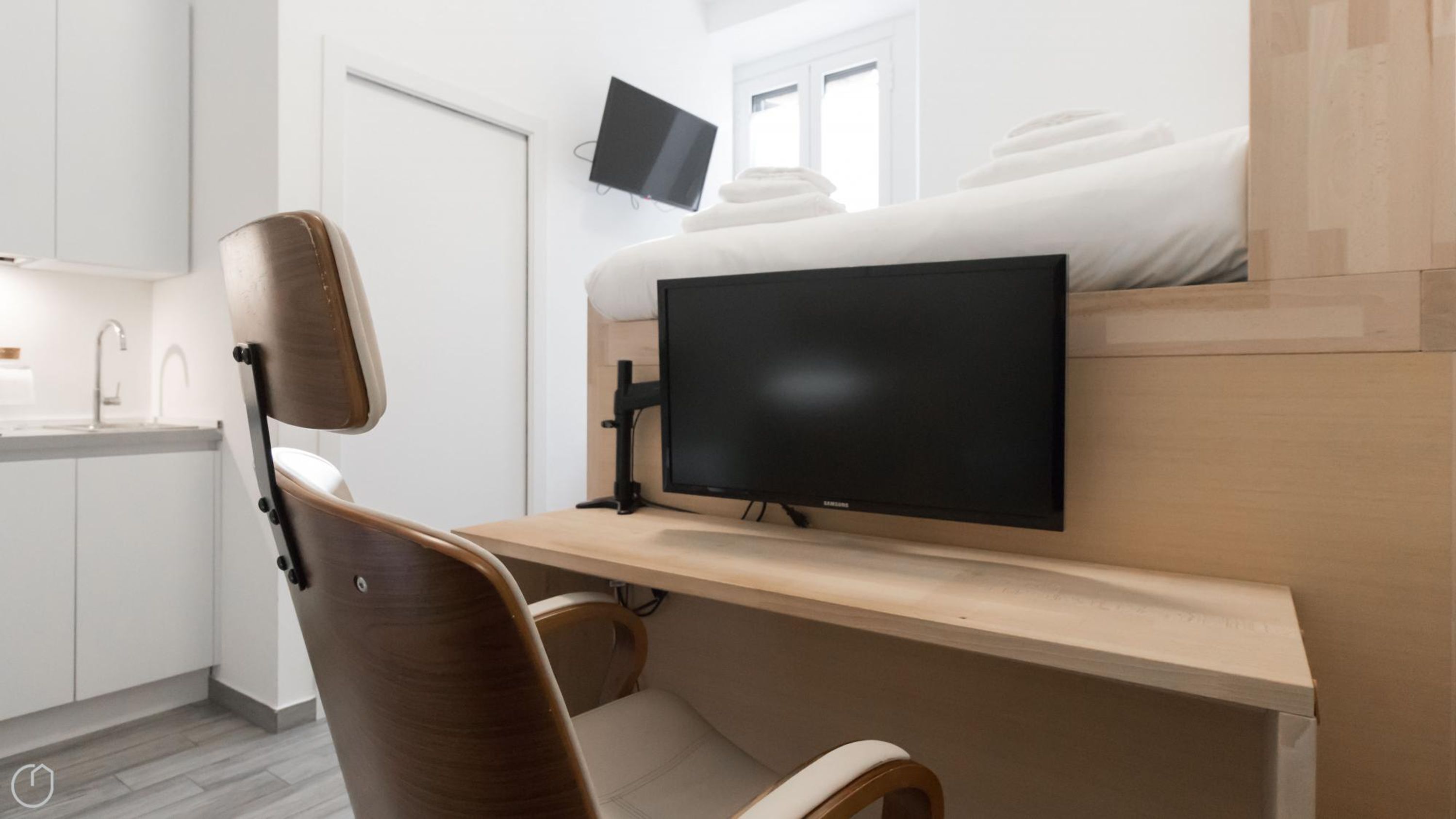 Una habitación de hotel moderna con una cama litera, un escritorio con televisor de pantalla plana, una silla y una zona de cocina con fregadero.
