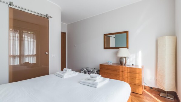 Quarto de hotel com uma cama grande, cômoda de madeira, espelho e luminária.