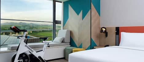A hotel room with a bed, a sofa, a bike, and a view of the countryside.