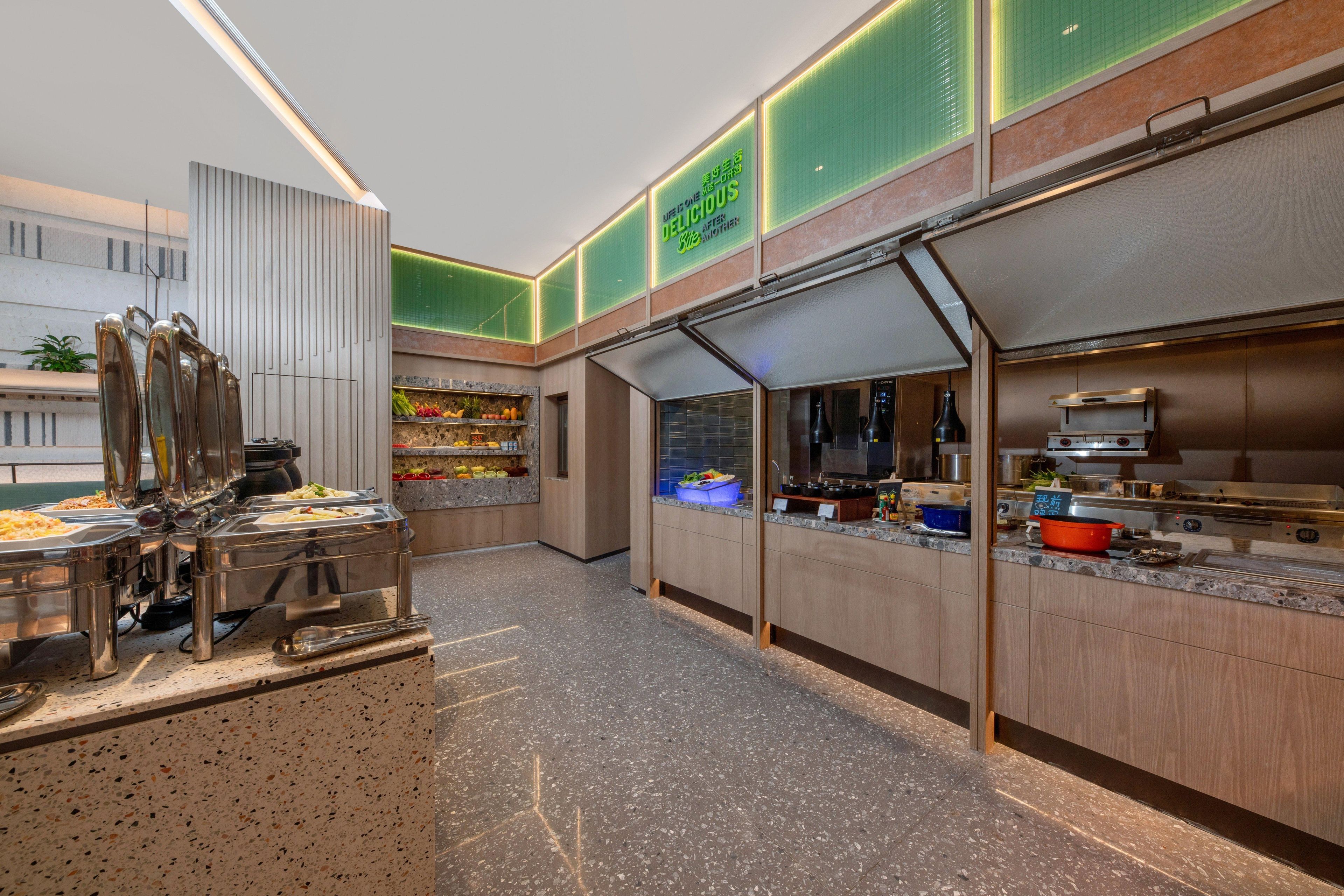 A modern kitchen area with stainless steel appliances, a buffet setup, and a green illuminated sign.