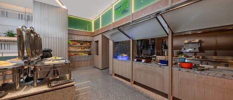 A modern kitchen area with stainless steel appliances, a buffet setup, and a green illuminated sign.