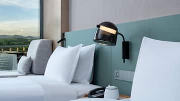 Quarto de hotel com cama, mesa de cabeceira, luminária e vista para uma ponte e montanhas.