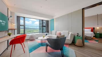 Quarto de hotel moderno com uma janela grande, um sofá, uma cadeira, uma mesinha e uma cama.