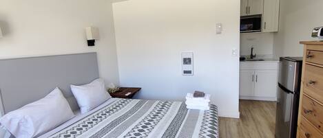 Ett sovrum med en säng, ett sängbord och ett litet sidobord. Det finns ett litet pentry med ett kylskåp och en mikrovågsugn.