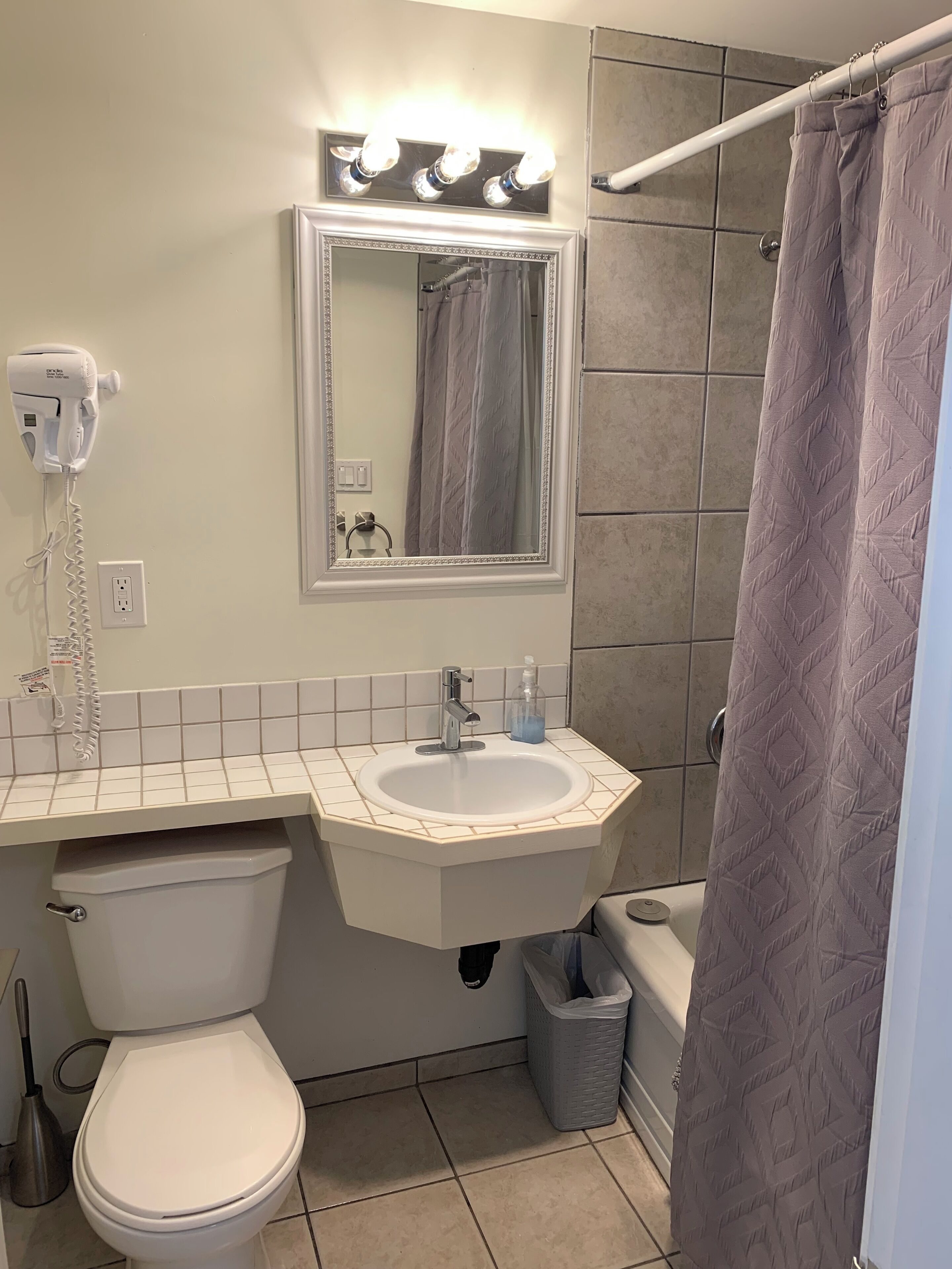 A bathroom with a white sink, a mirror above it, a hairdryer on the wall, and a shower curtain.