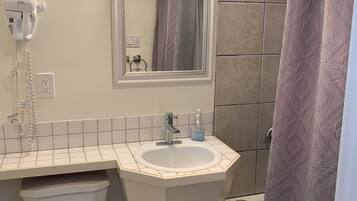 A bathroom with a white sink, a mirror above it, a hairdryer on the wall, and a shower curtain.