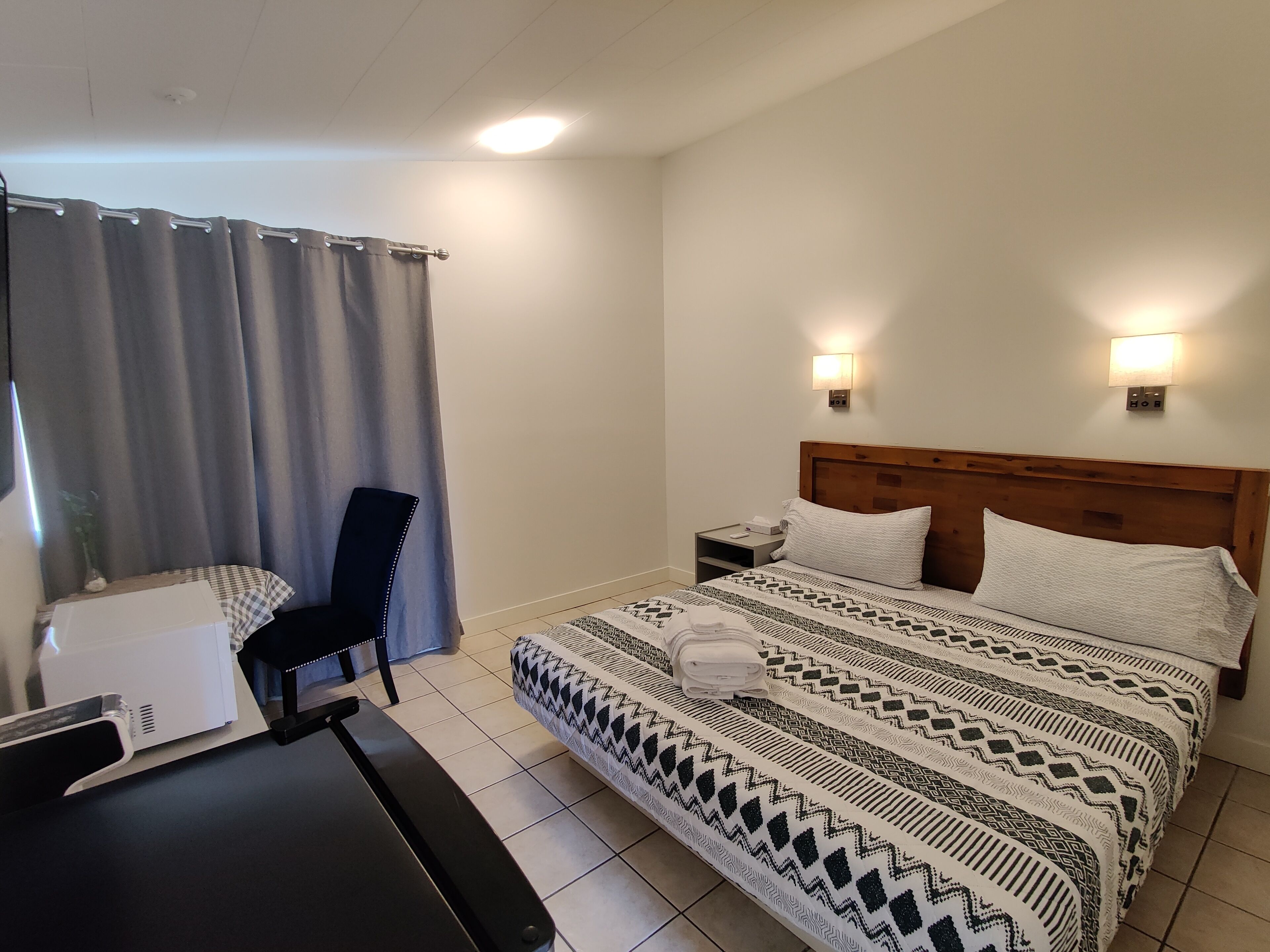 Een hotelkamer met een bed, nachtkastje, stoel en een bureau met een computer.