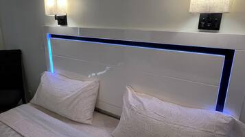Habitación de hotel con cama, dos lámparas de noche y un cabecero moderno con iluminación azul.