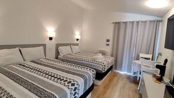A hotel room with two beds, a small desk, a mirror, and a window with curtains.