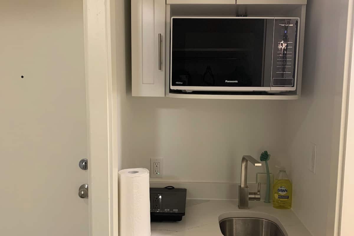 A compact kitchen with white cabinets, a microwave, a sink, a faucet, a roll of paper towels, and a bottle of Dawn dish soap.