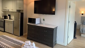 Una cocina moderna con electrodomésticos de acero inoxidable, un televisor de pantalla plana montado en la pared y un aparador de madera oscura con cajones.