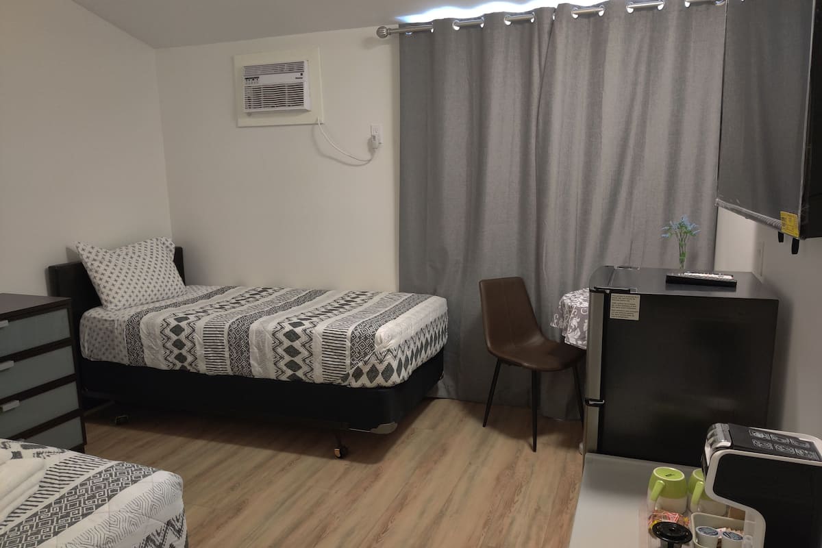 A compact room with a bed, a desk, a chair, and a small kitchenette area.