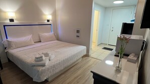 Un dormitorio con cama, lámparas de noche, una mesita de noche con un jarrón y una puerta que da a otra habitación.
