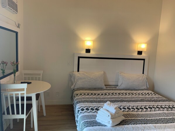 A hotel room with a bed, two bedside lamps, a small table with a chair, and a vase with flowers.