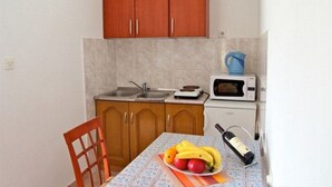 Une petite cuisine avec des meubles en bois, un four à micro-ondes, une bouilloire et une table sur laquelle se trouvent des fruits et une bouteille.