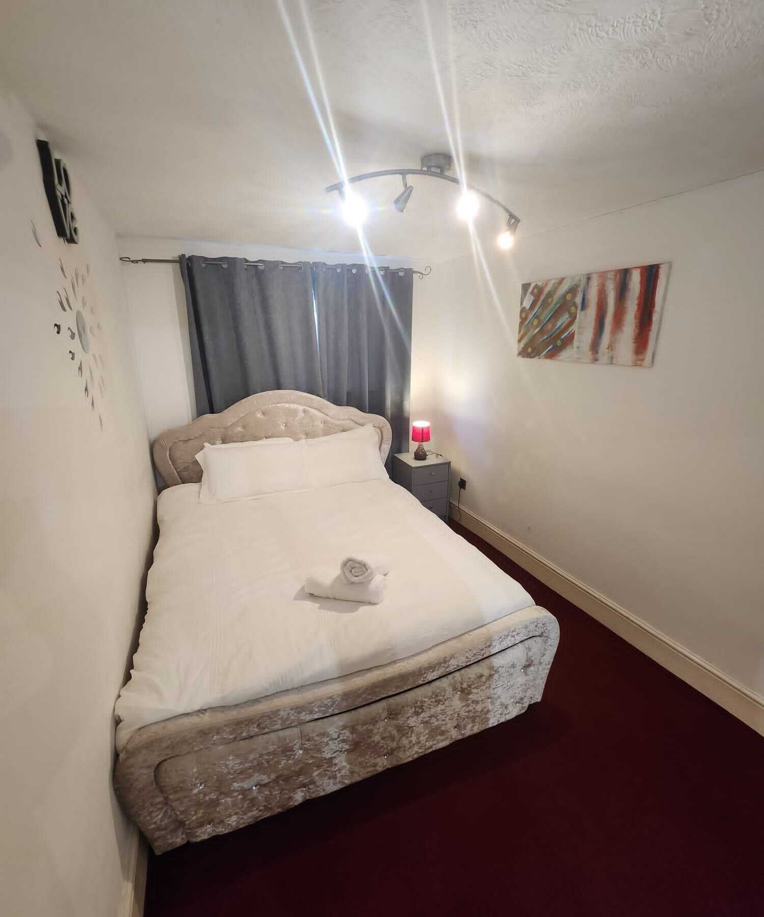 A neatly made bed with a headboard, a bedside lamp, and a wall art piece.