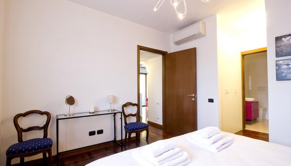 Quarto de hotel com uma cama, duas cadeiras, uma escrivaninha e um espelho.