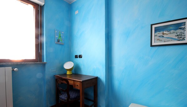 A room with blue walls, a wooden chair, a small table, a window, and a framed picture on the wall. - Italianway Easy - Rucellai 37 (Milan)