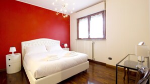 A bedroom with a white bed, red walls, a wooden floor, a glass table, and a window with curtains. - Italianway Easy - Rucellai 37 (Milan)