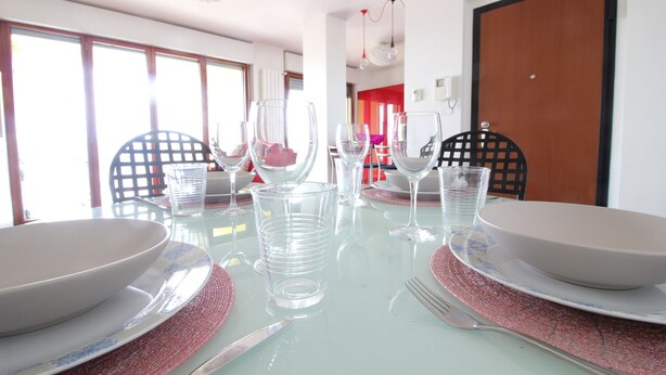 A dining table set with clear glassware and plates, surrounded by chairs. - Italianway Easy - Rucellai 37 (Milan)