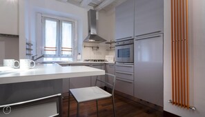 Une cuisine moderne dotée d’un îlot central, d’appareils électroménagers en acier inoxydable et d’une fenêtre avec des stores.