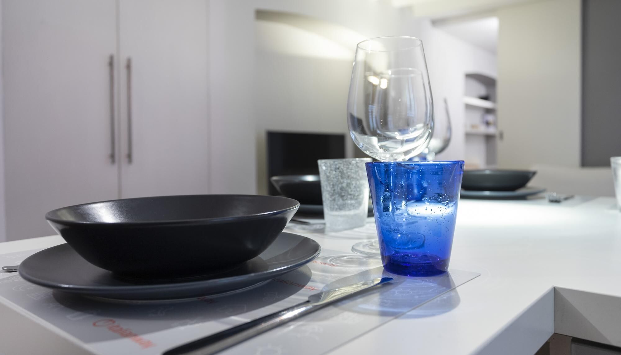 Una cocina moderna con un tazón negro sobre una encimera blanca, un vaso azul y otro transparente.