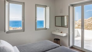 A bedroom with two beds, a window with a view of the sea, a mirror, and a small shelf with items. - Epic Twin Luxurious 14 Bedrooms Villa for 28 (Mykonos)