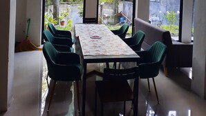 Una habitación con una mesa grande y sillas, ventanas amplias con vistas a zonas verdes, e iluminación en el techo.