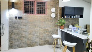 Una cocina con paredes de ladrillo, luces colgantes, una planta en maceta, una barra con taburetes y un reloj en la pared.
