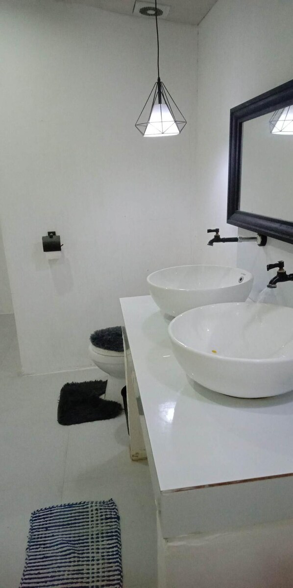 Un baño moderno con dos lavamanos blancos, un grifo negro, un inodoro blanco y una alfombra negra.
