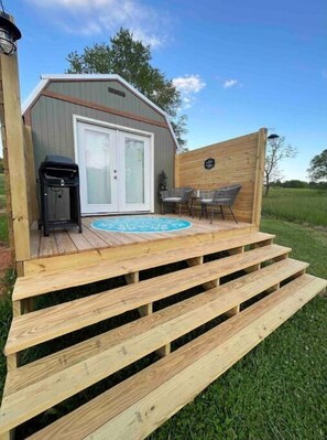 Une terrasse en bois avec un jacuzzi, un barbecue et un espace extérieur aménagé avec des chaises et une table.